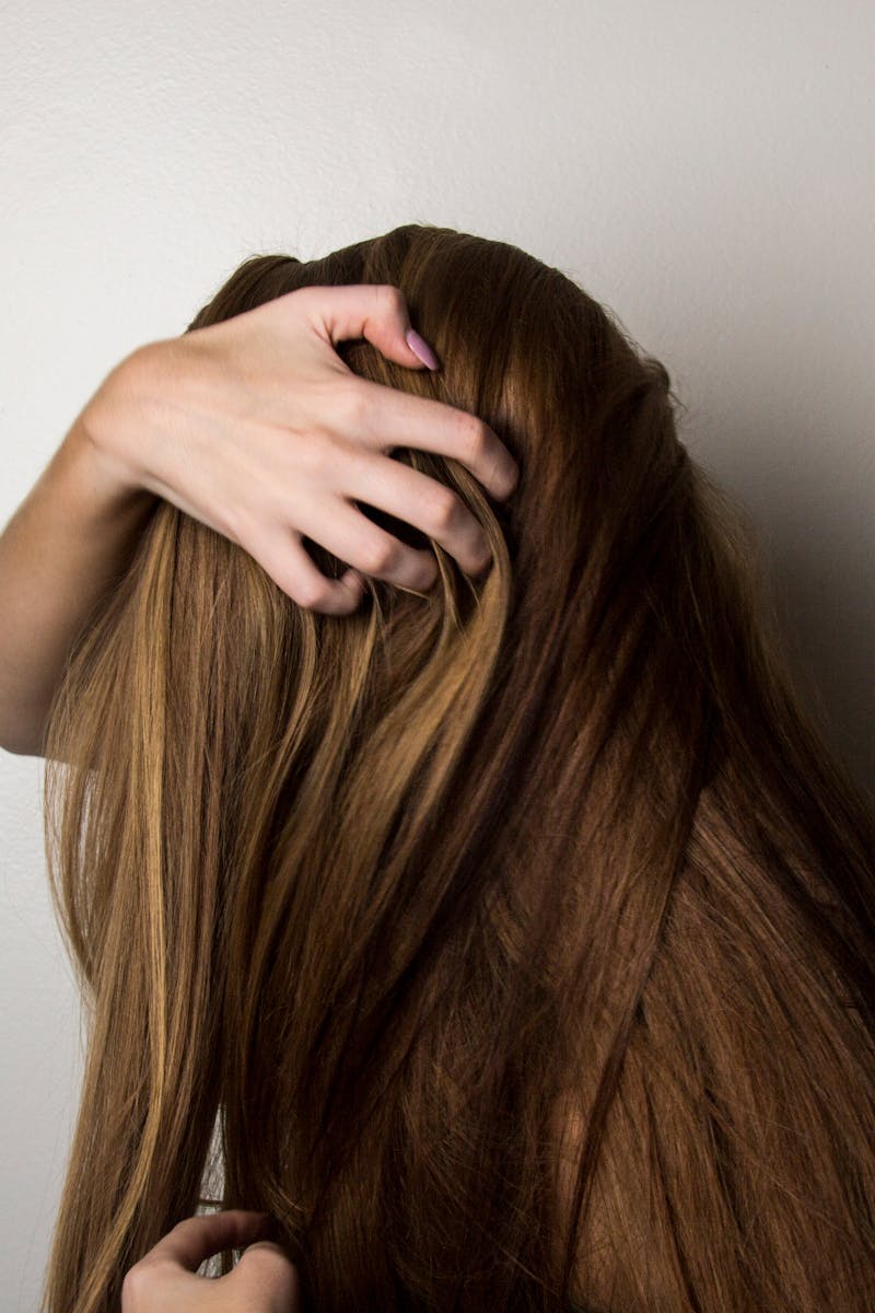 An artistic close-up of a woman's long brunette hair held gently by her hand, emphasizing texture and color.