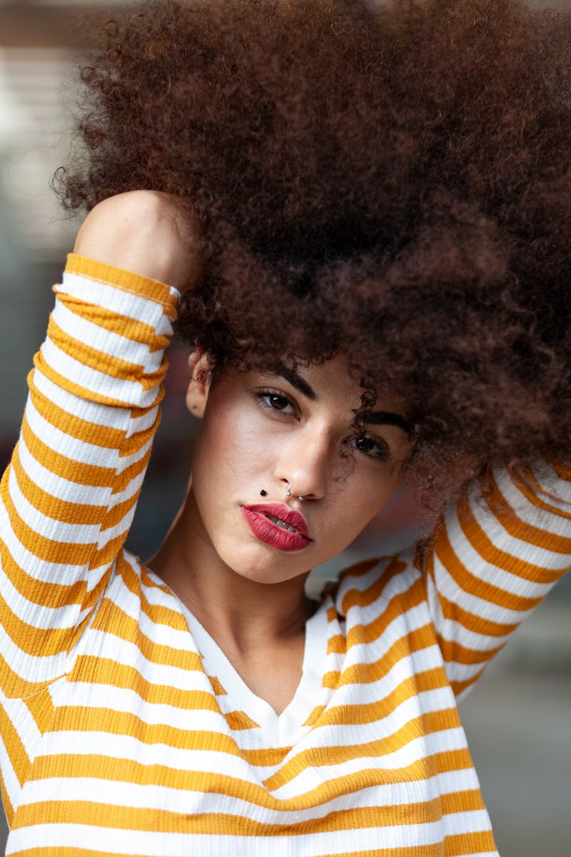 Close-up portrait of a stylish woman with afro hair and red lips posing.